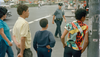 Three boys stand at a street corner while a police officer crosses the street